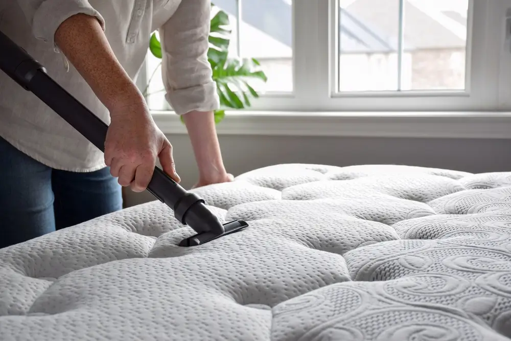 Femme utilisant un aspirateur pour aspirer un matelas dans une chambre.