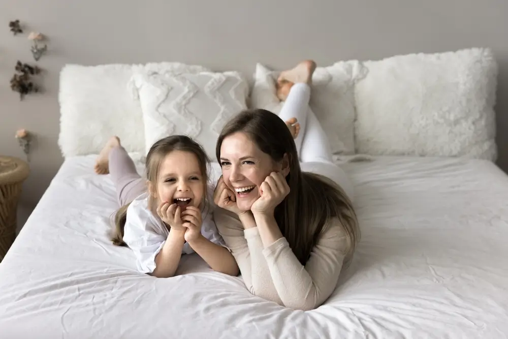 Jeune femme et sa petite fille de 4 ans parlent et rient ensemble, allongée sur le lit.