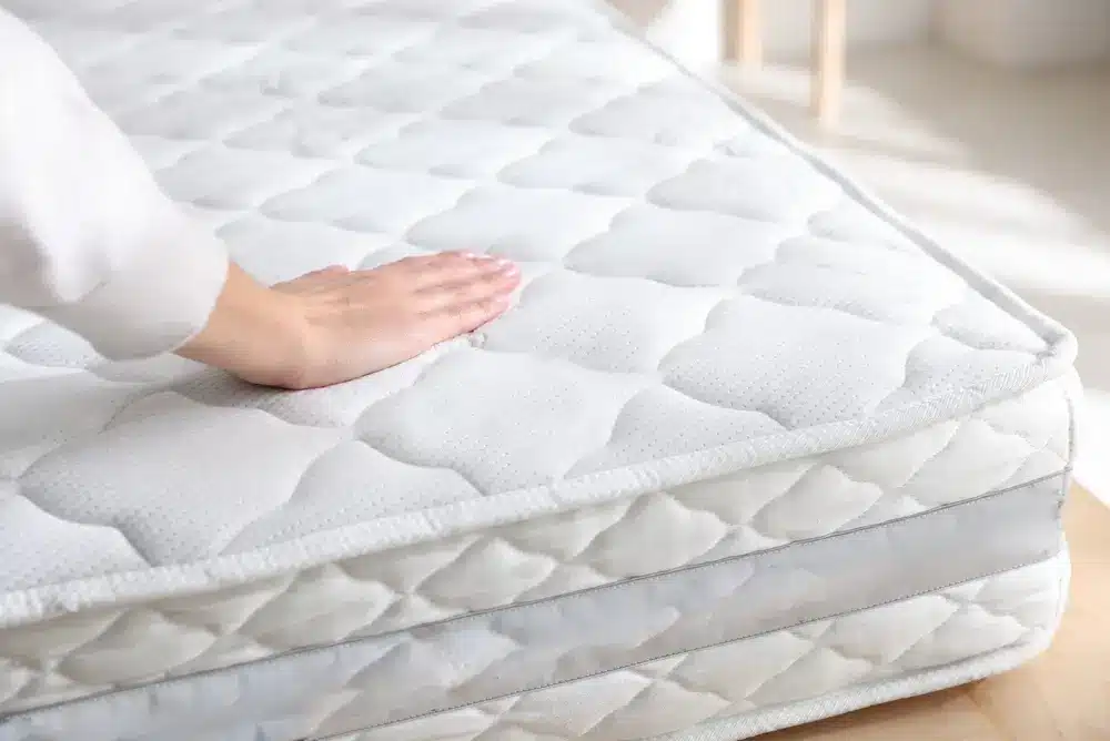 Femme touchant un matelas mou sur le lit à l'intérieur, gros plan.