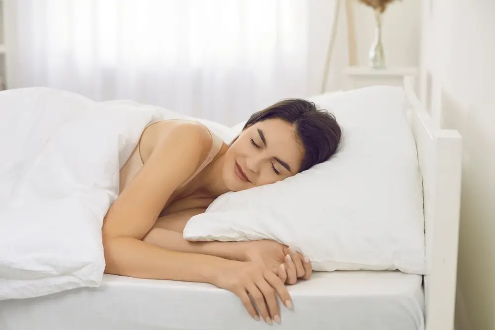 Une jeune femme calme, allongée dans un confortable lit blanc, fait un rêve matinal sain et endormi.