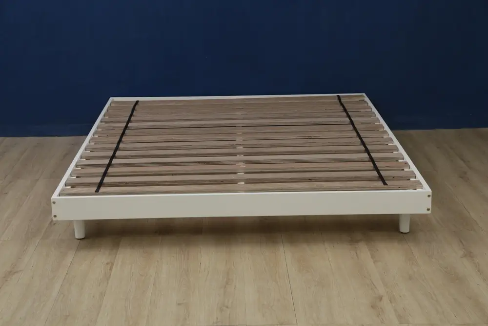 Un simple cadre de lit en bois blanc avec une base en tissu de couleur neutre.